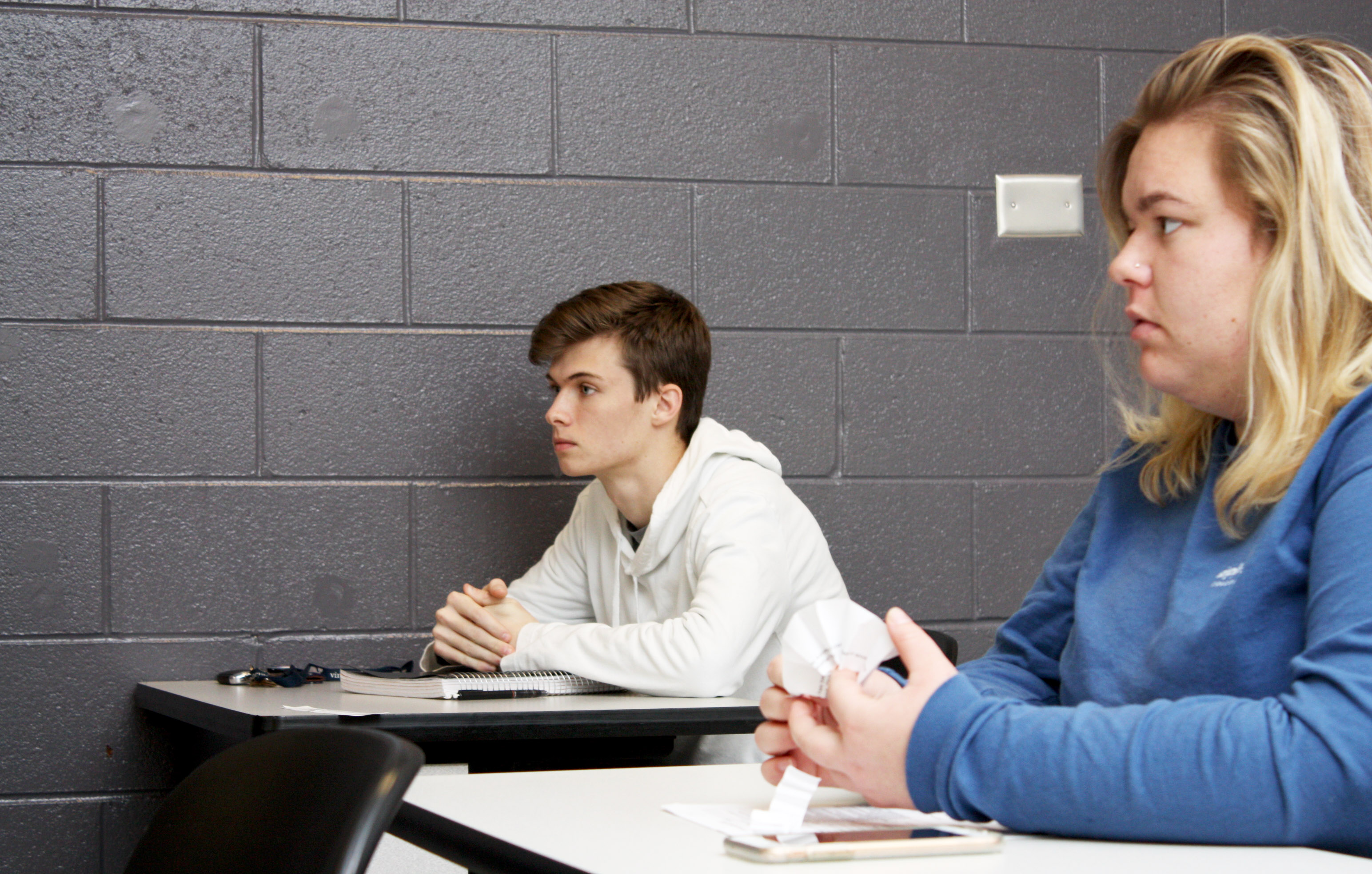 A male student sits at a desk with a female student to the right.