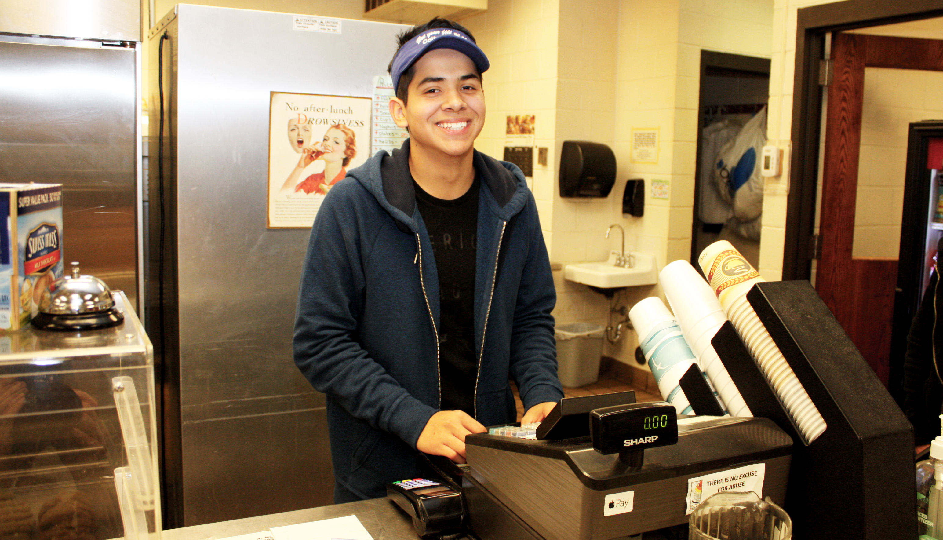 Andres Rodriguez behind the register at the Campus Grill. The diligent student will finish his program a year early, with an extra degree, and manages a part-time job.