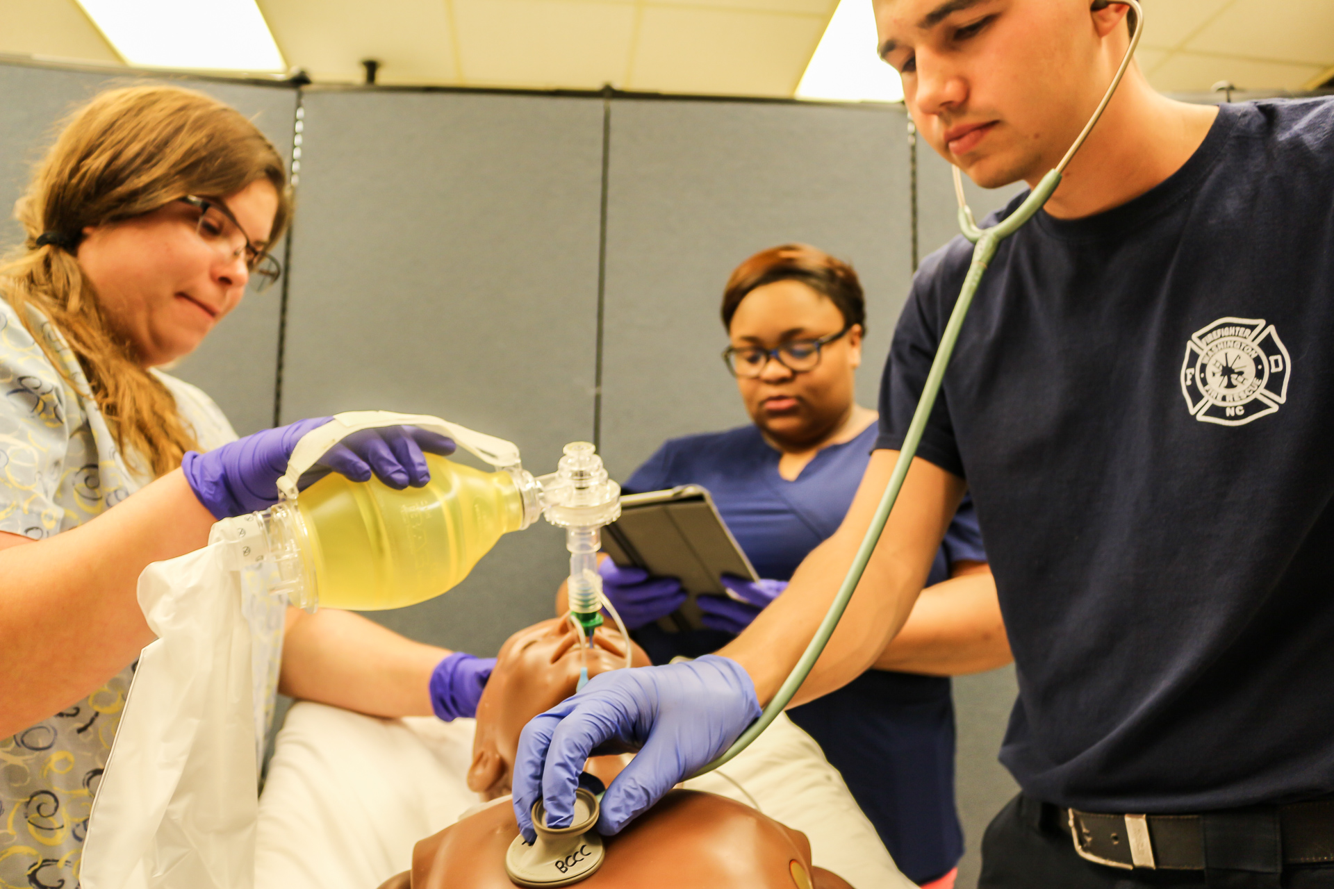 One student uses a stethoscope on a dummy while another ventilates it.