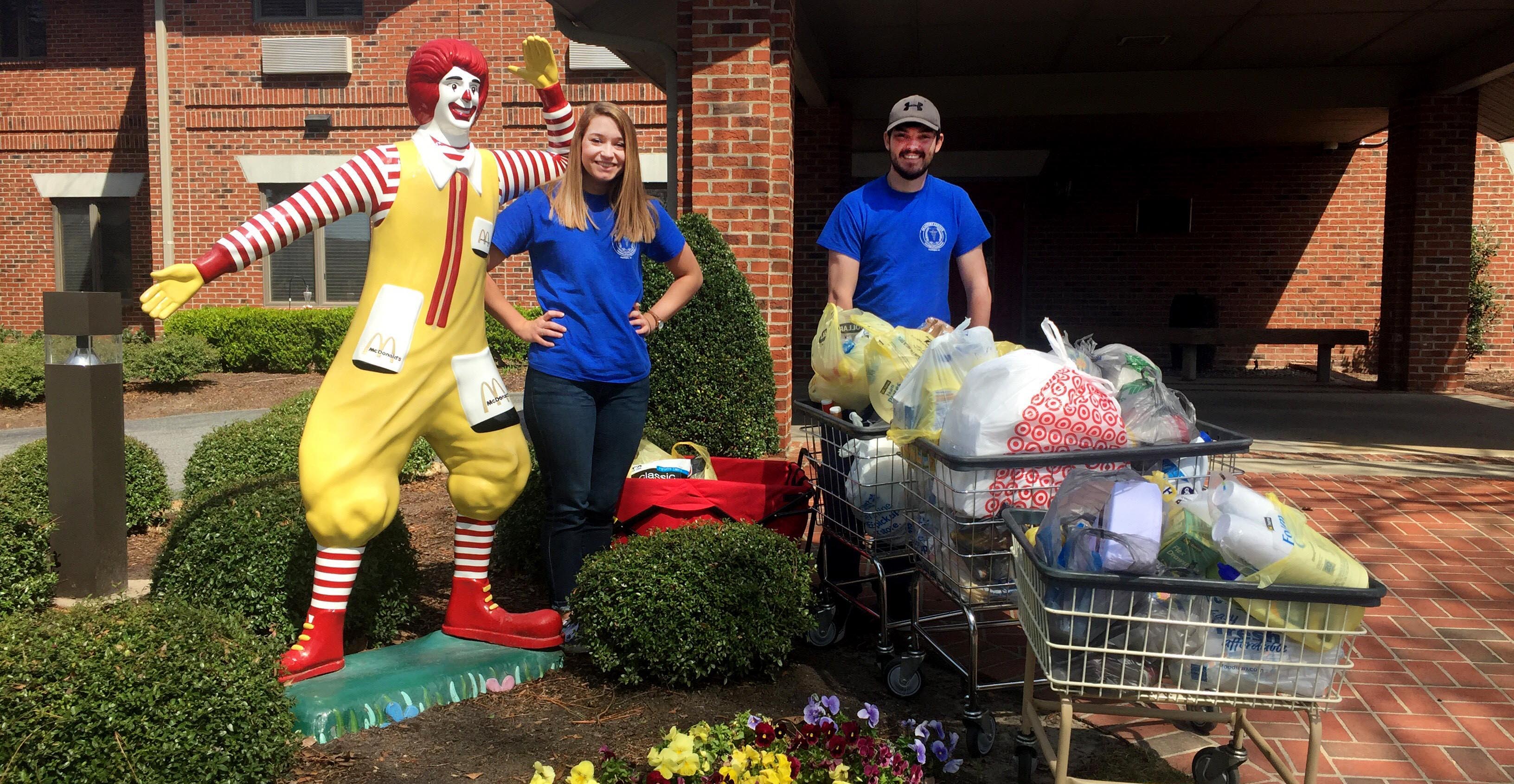 Two students stand with donations and a statue of Ronald McDonald.